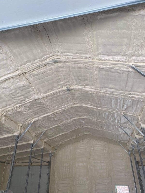 An interior view of a room with walls and a vaulted ceiling covered in beige spray foam insulation.