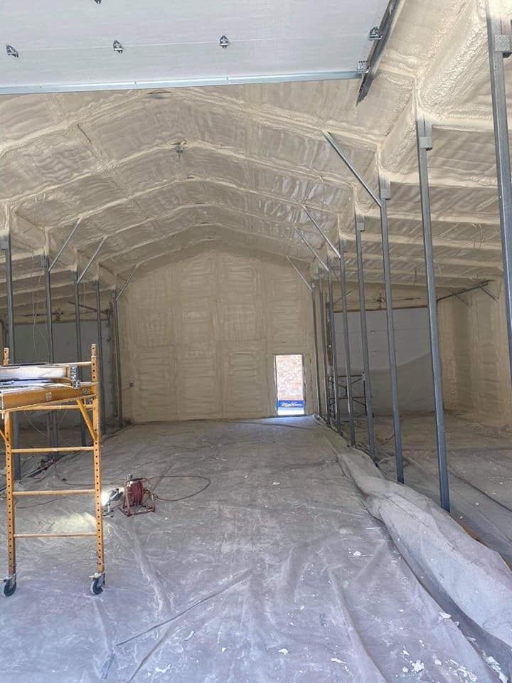 Interior of a large building with walls and ceilings coated in textured, light-colored spray foam insulation.