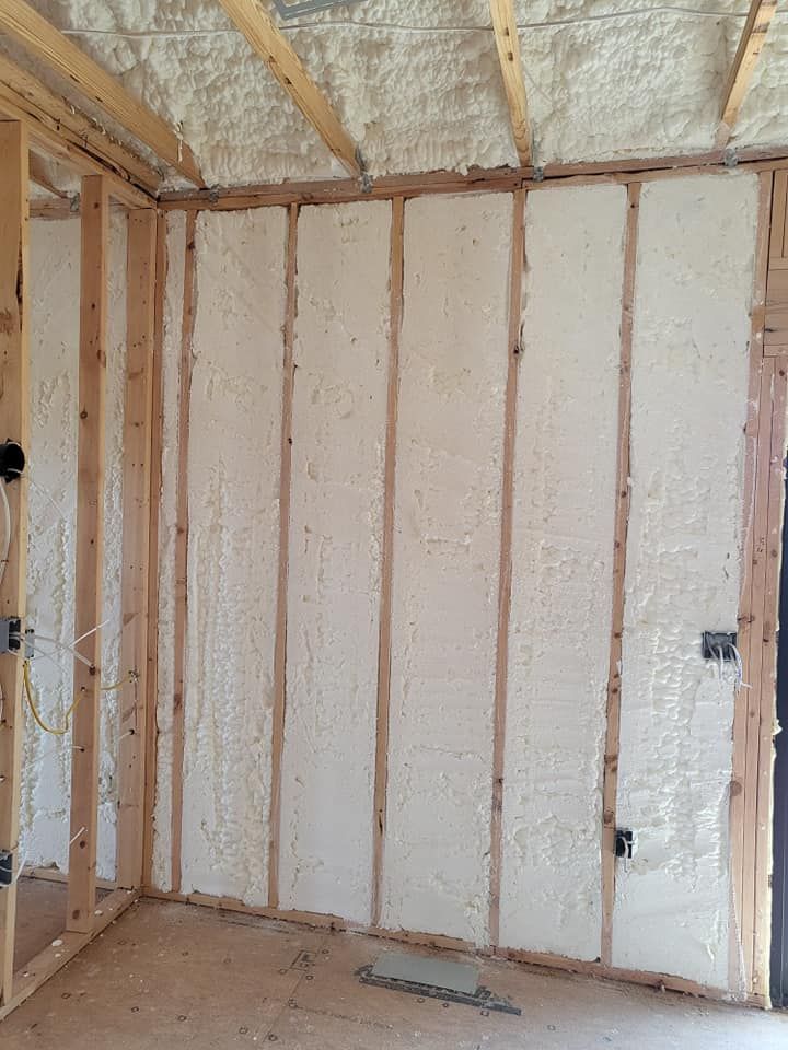 Interior wall studs and ceiling joists insulated with white spray foam in a room under construction.