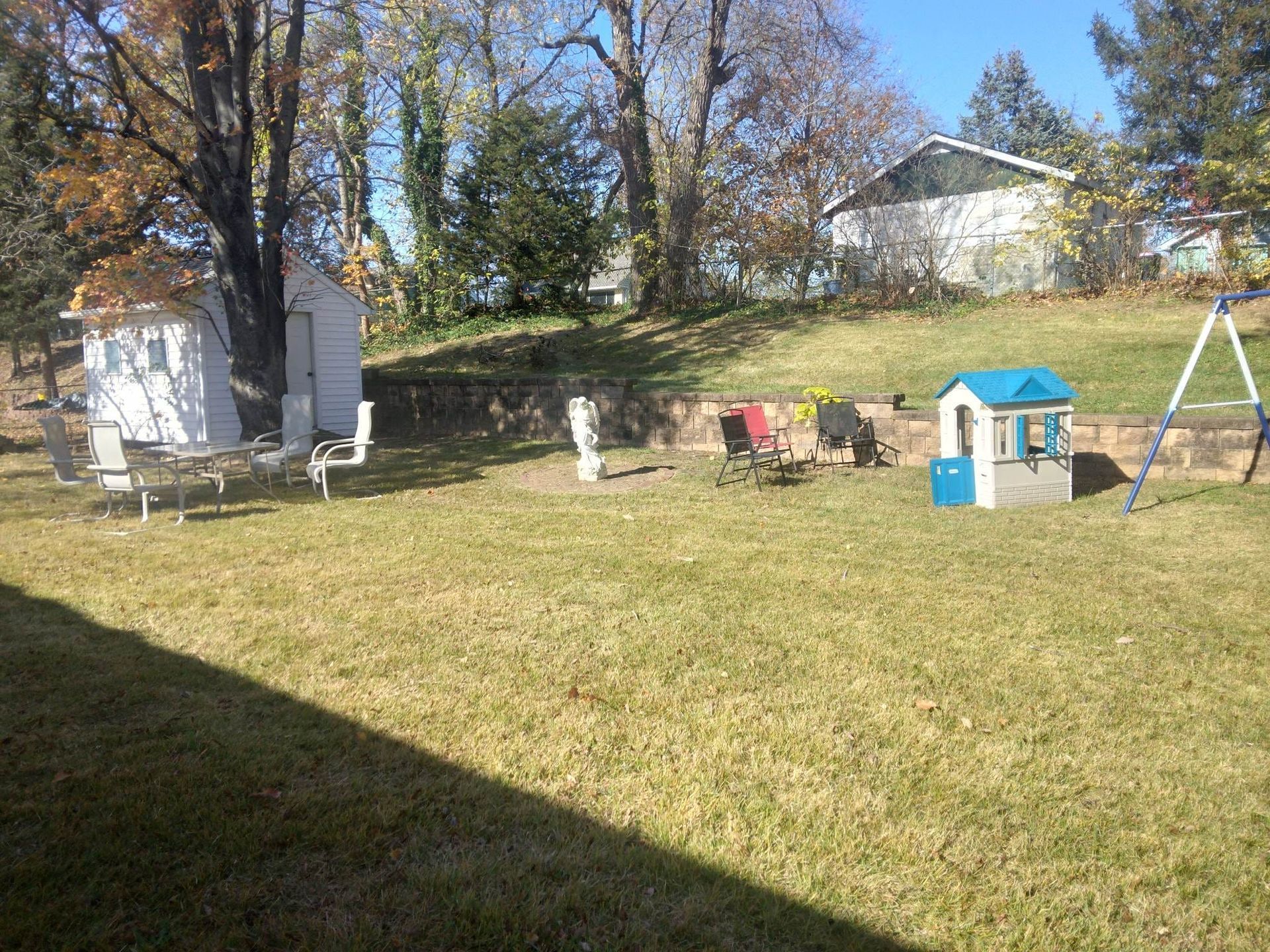 A backyard with a playhouse, swings, and a shed.