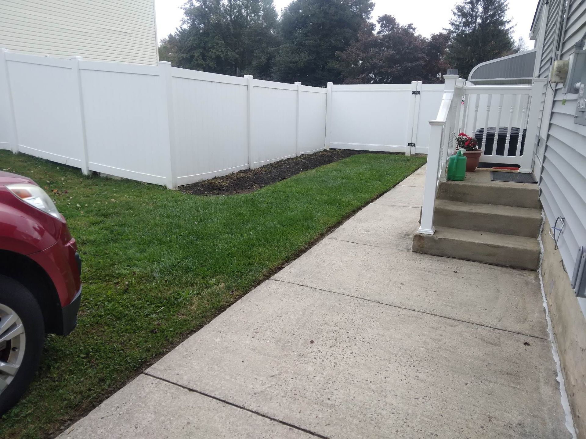A red car is parked in front of a white fence