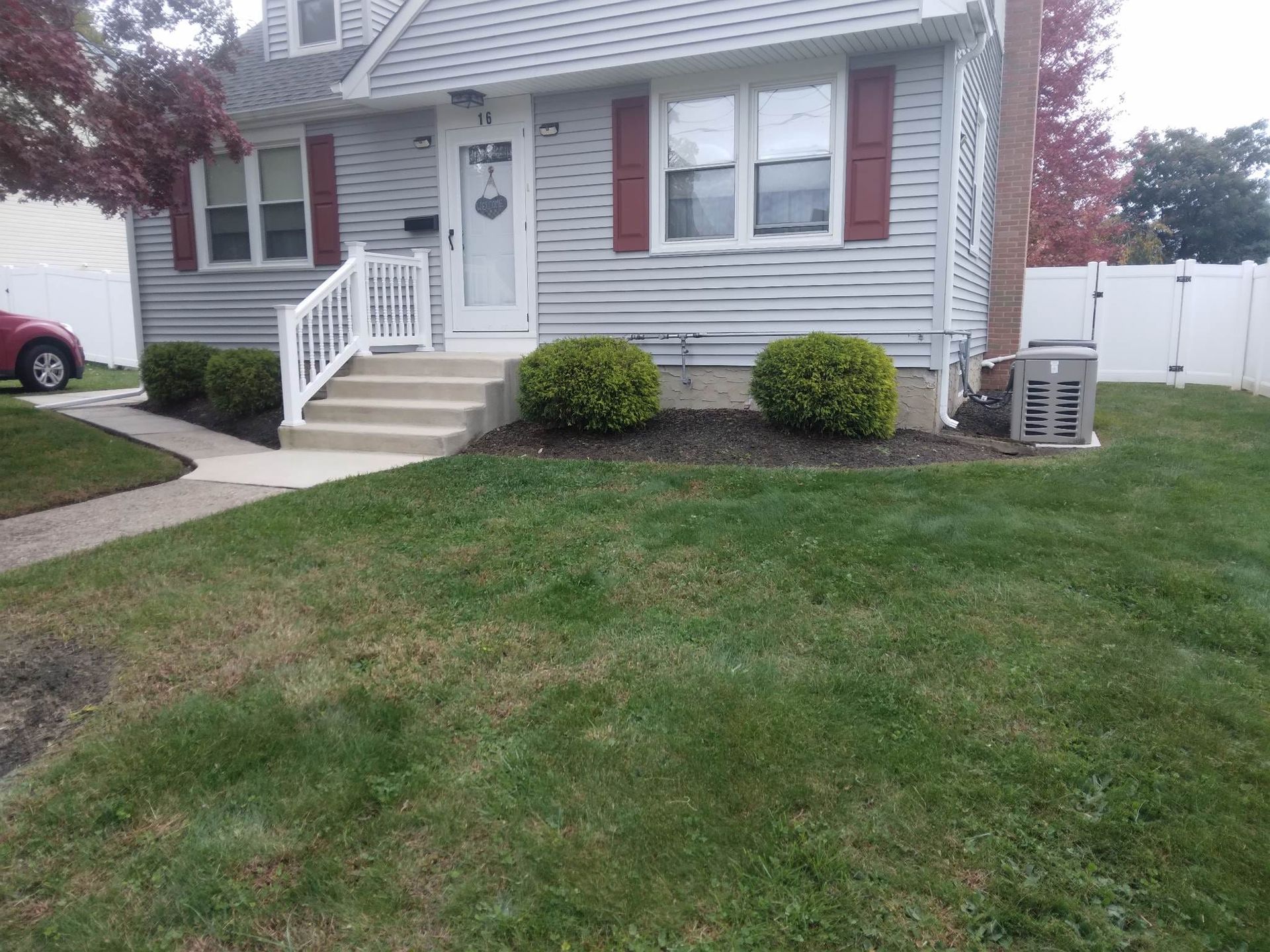 A house with a lush green lawn and a red car parked in front of it.