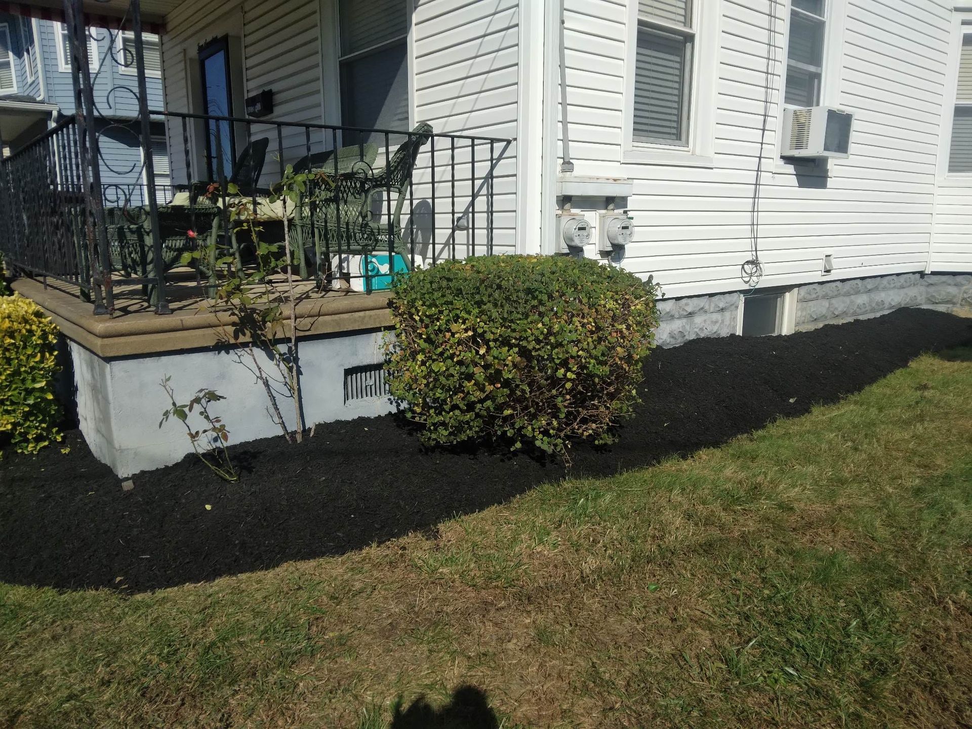 A white house with a porch and black mulch in front of it