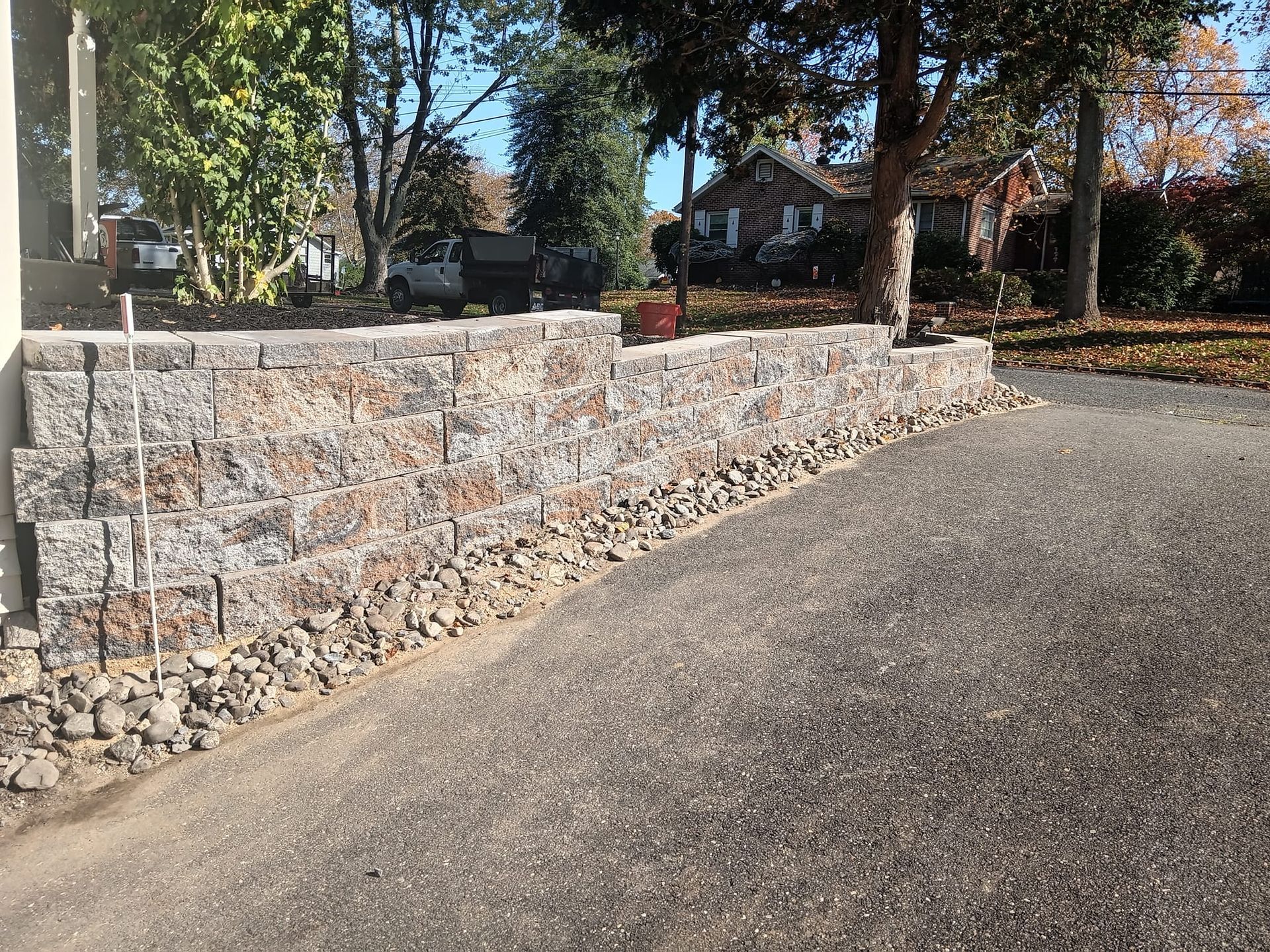 A stone wall along the side of a driveway next to a house.