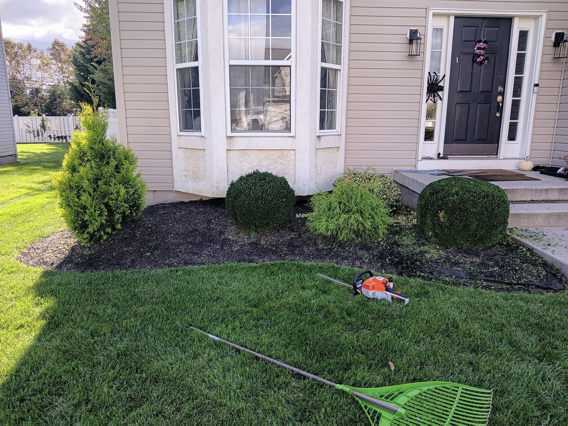 A green rake is sitting in the grass in front of a house.