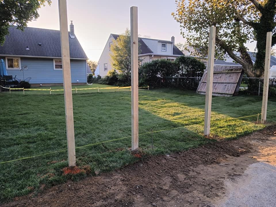 A fence is being built in a yard with a house in the background.