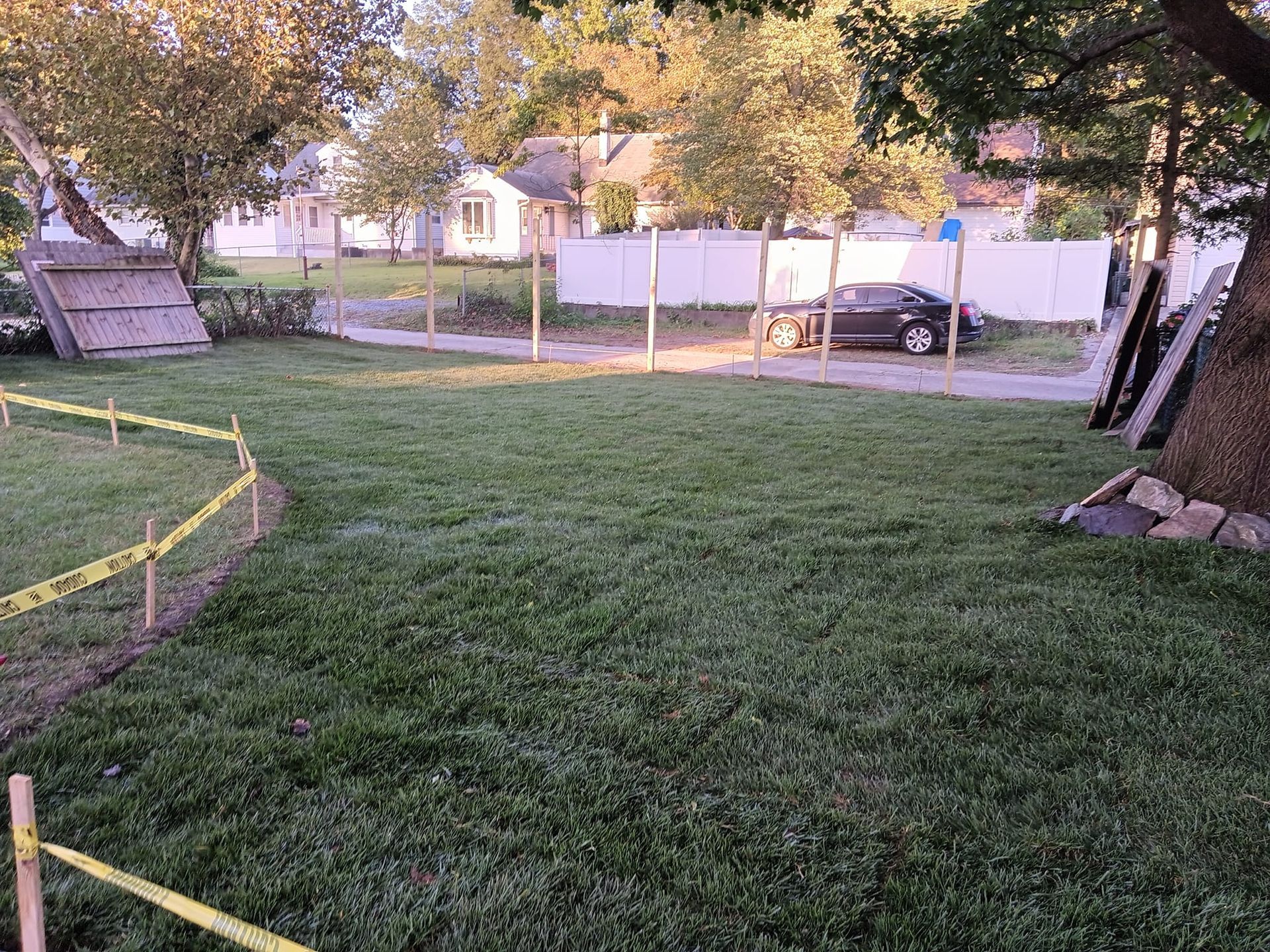 A lush green lawn with a fence and a car parked in the background.