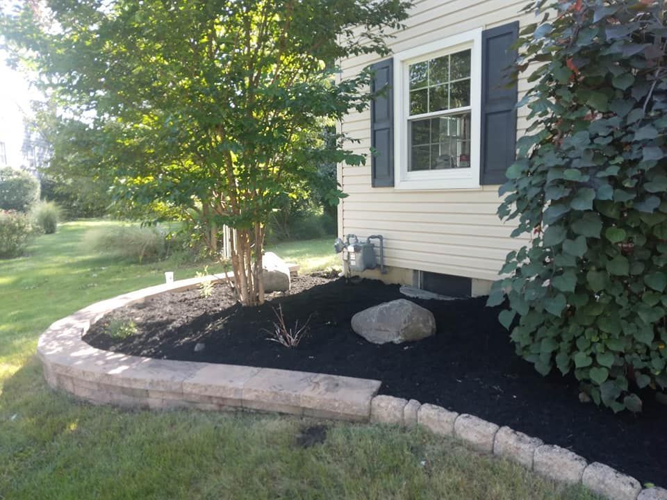 A house with black shutters and a black mulch bed in front of it.