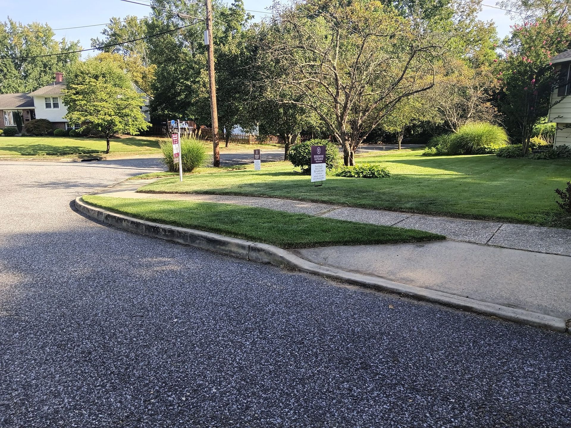 A corner of a street with a sidewalk and a grassy yard.