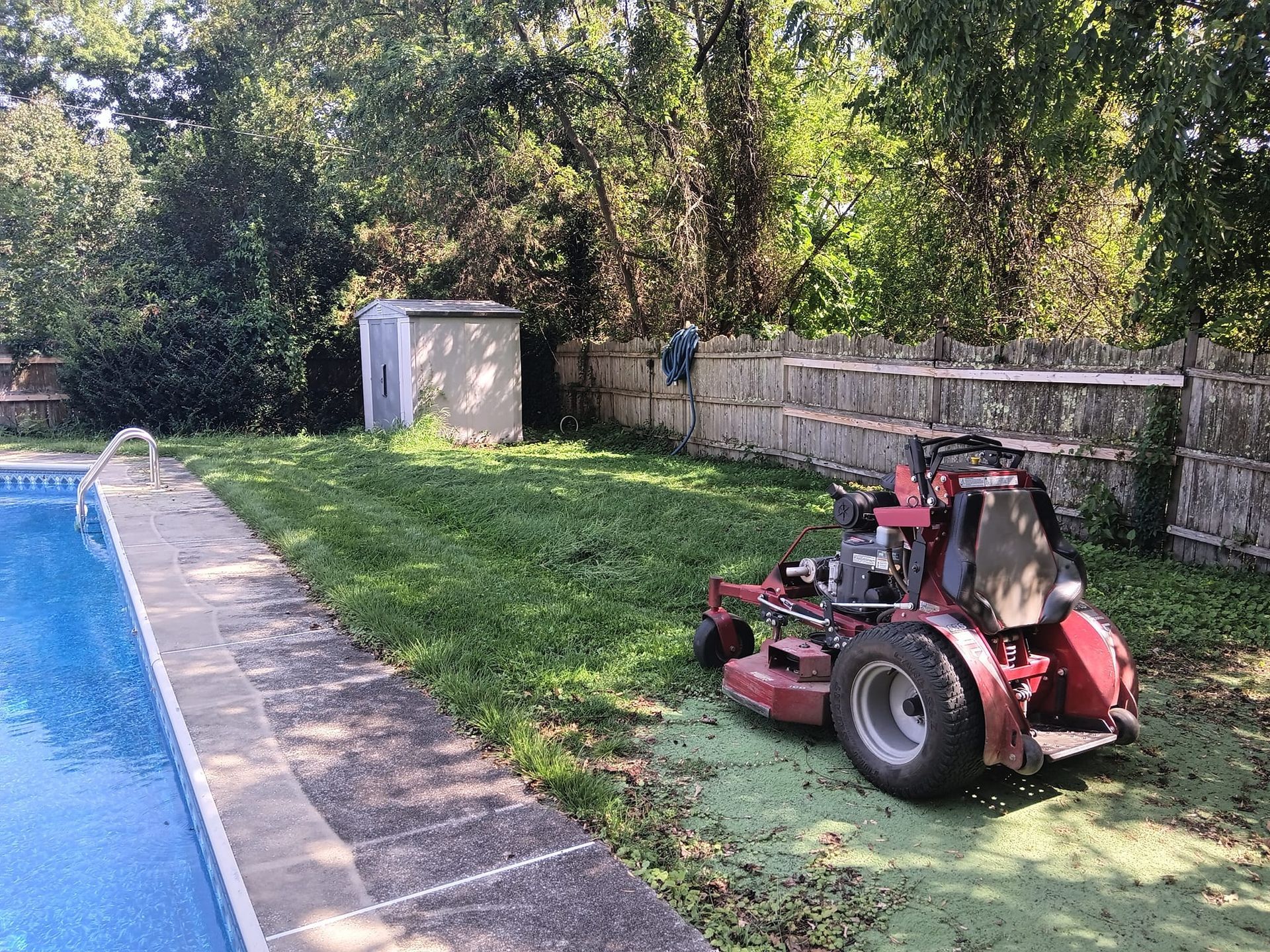 A lawn mower is parked in a backyard next to a pool.