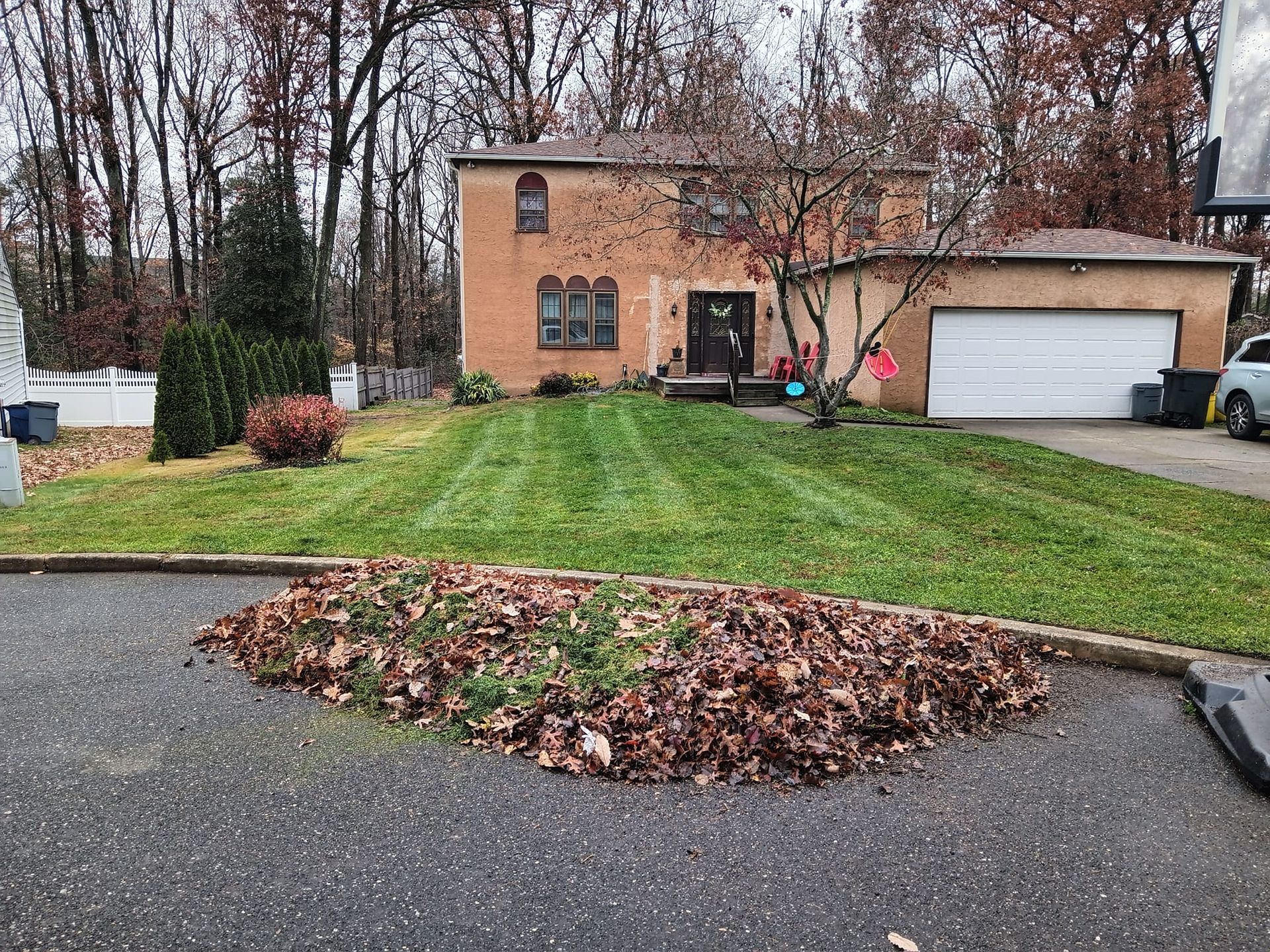 A house with a lush green lawn and a pile of leaves in front of it.