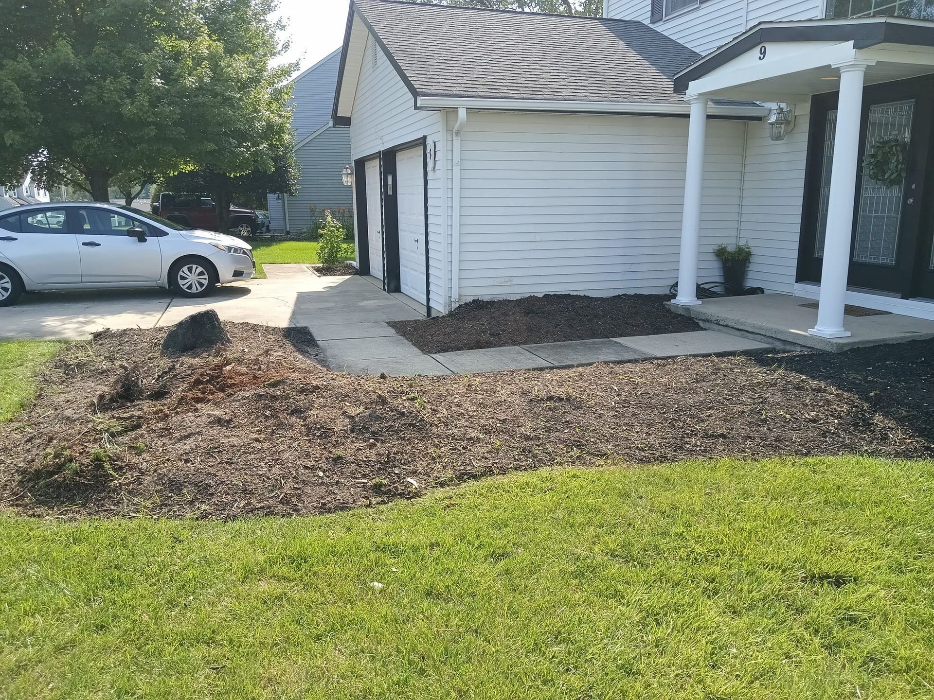 A white car is parked in front of a white house.