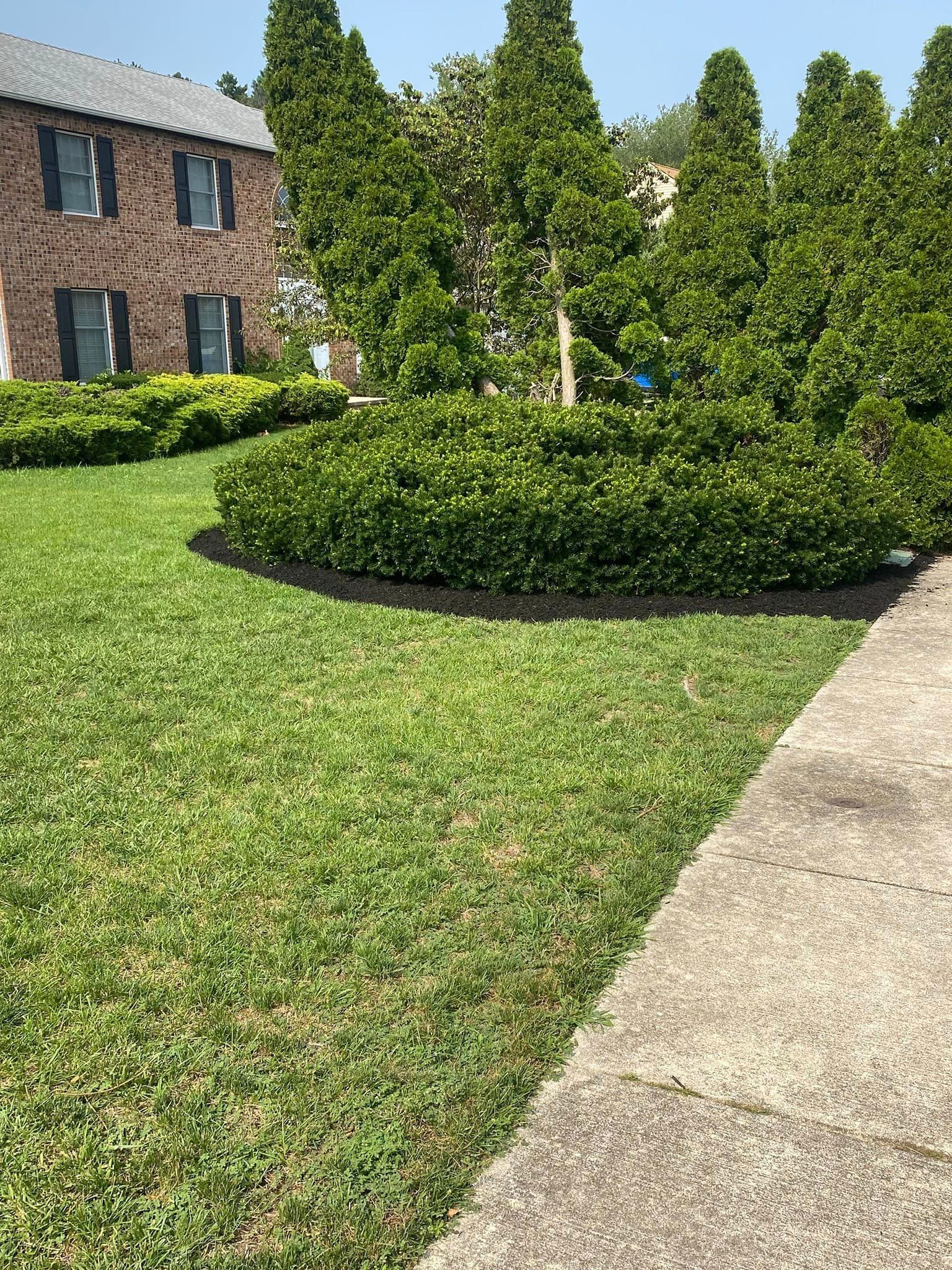A brick house with a lush green lawn and bushes in front of it.