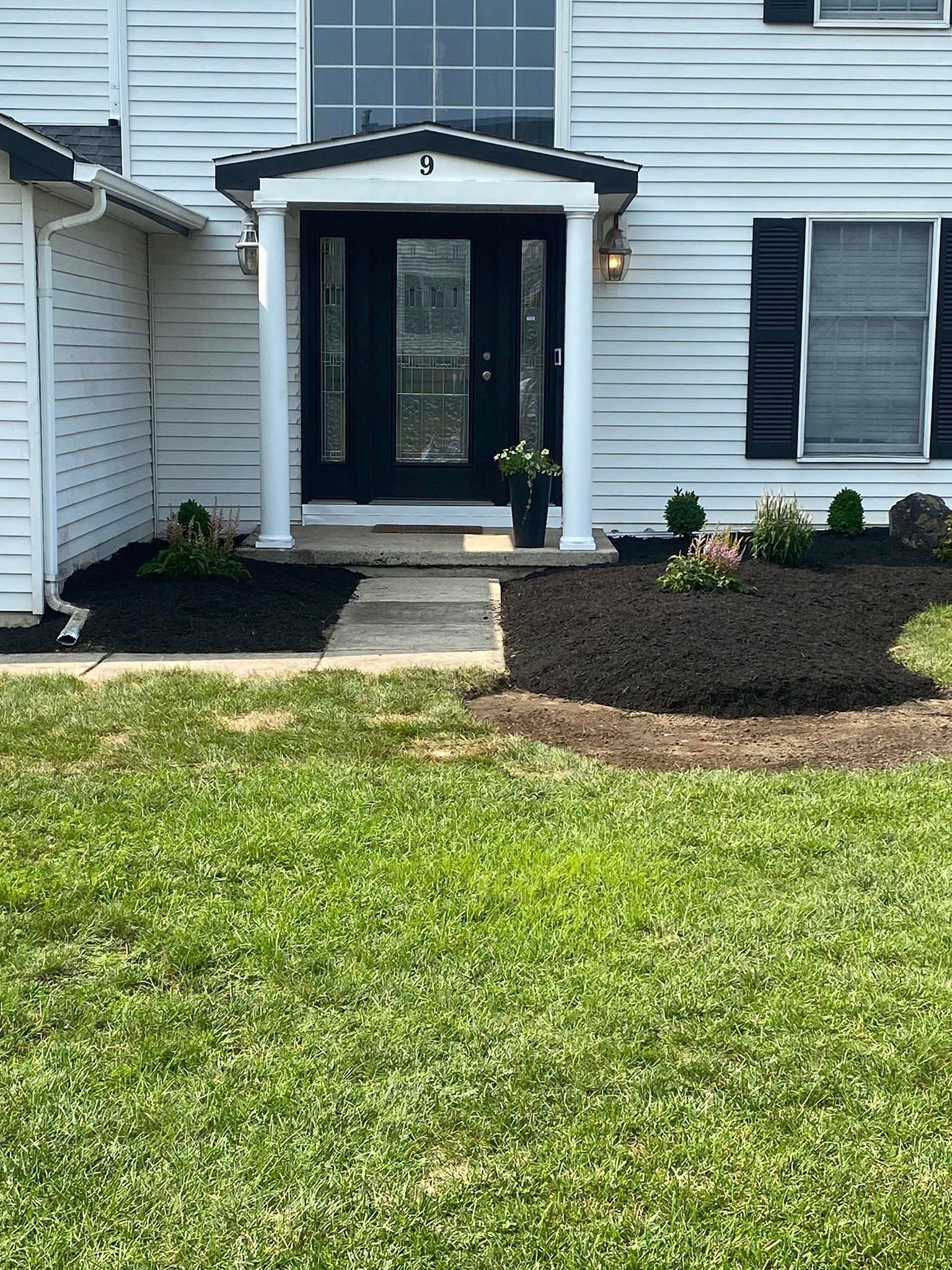 A white house with a black front door and a lush green lawn in front of it.