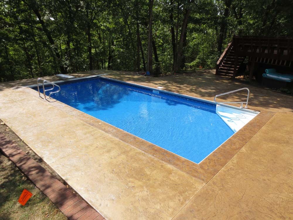 A large swimming pool is surrounded by trees and a deck.