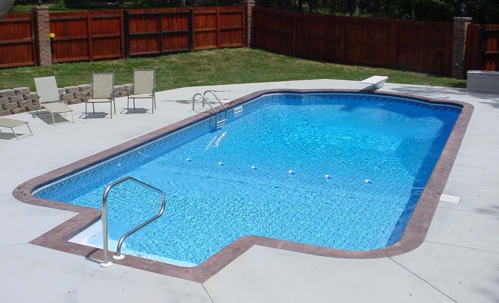 A large swimming pool is surrounded by chairs and a wooden fence.