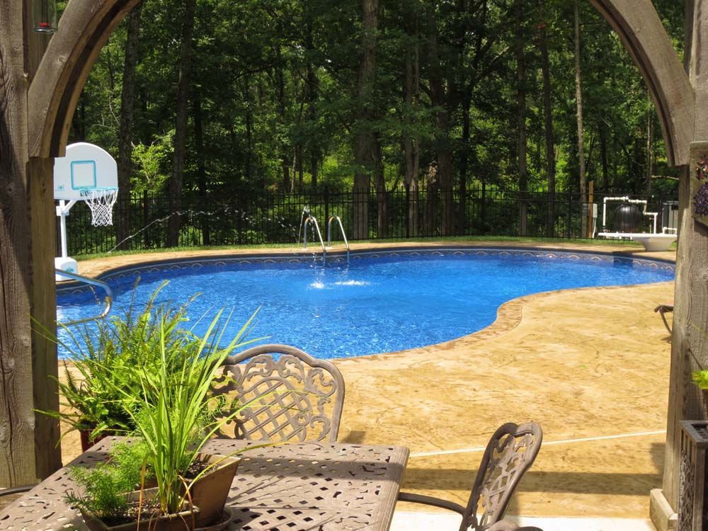 A large swimming pool is surrounded by trees and a table and chairs.