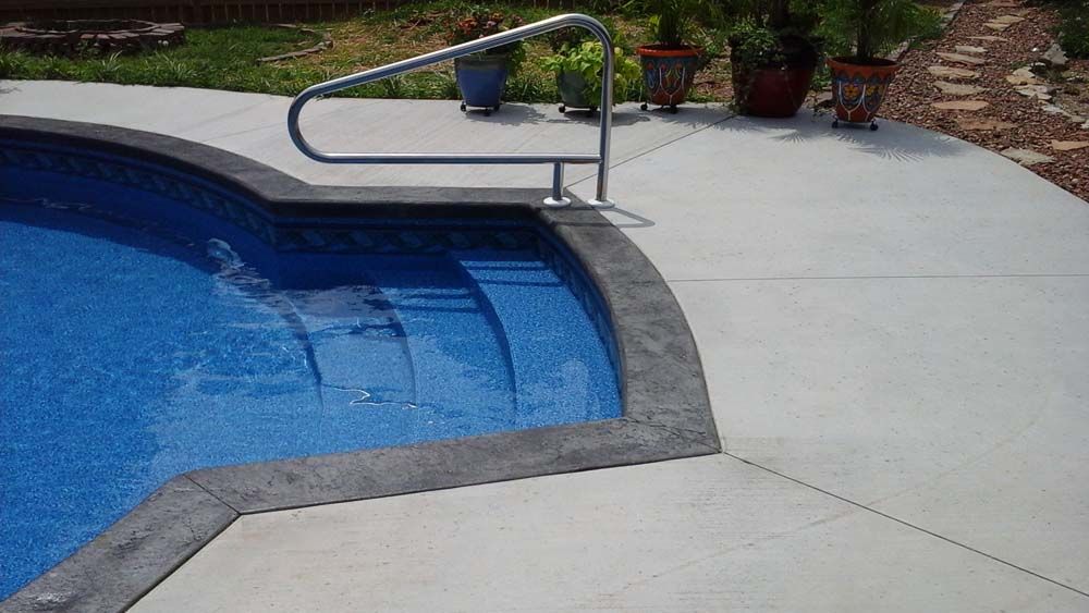 A swimming pool with a concrete deck and stairs leading to it.