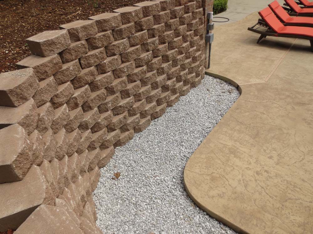 A brick wall next to a patio with red chairs