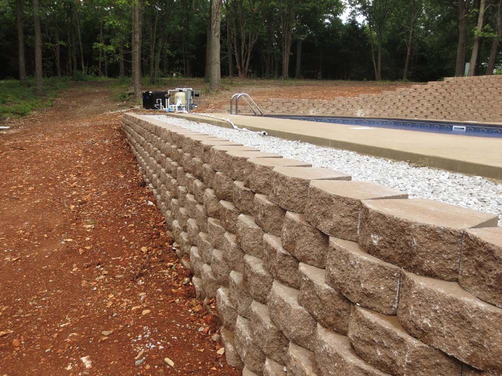 A large stone wall is surrounding a swimming pool.