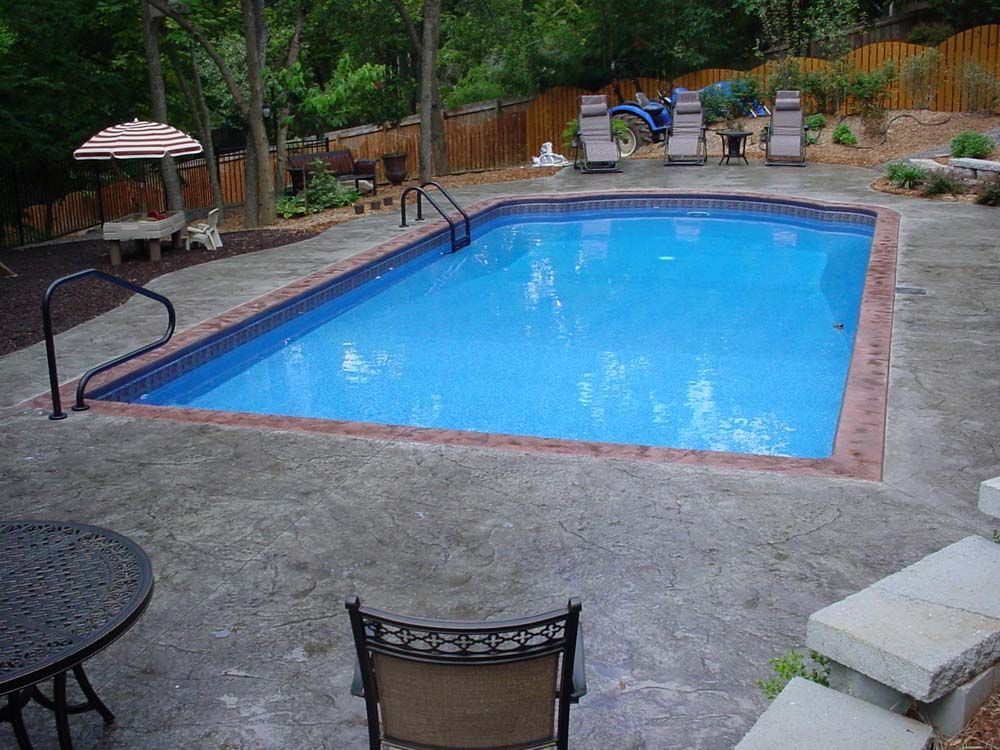 A large swimming pool is surrounded by chairs and a table