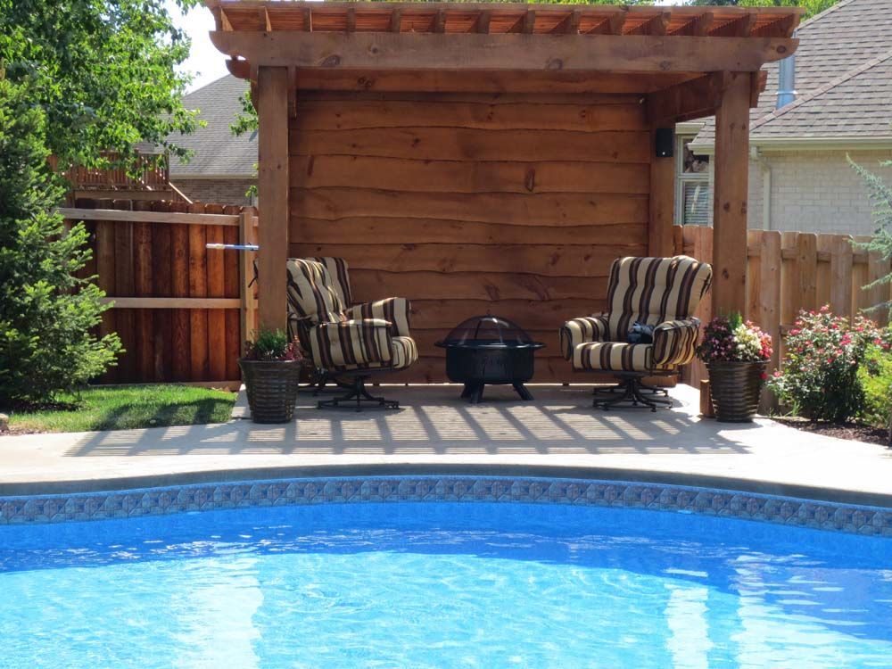 Two chairs are sitting under a wooden pergola next to a swimming pool.
