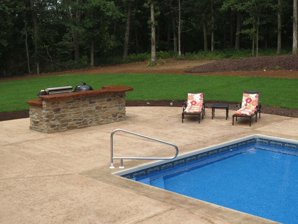 A swimming pool with a patio area with chairs and a grill