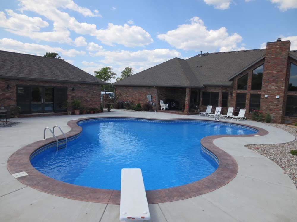 A large swimming pool with a diving board in front of a house