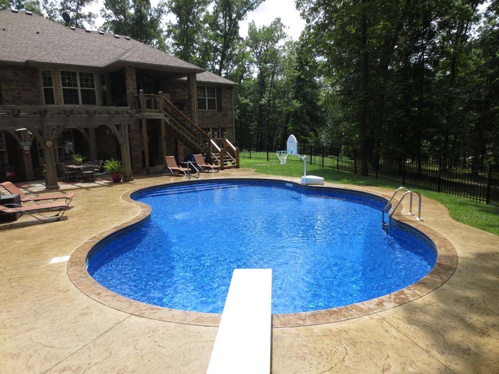 A large swimming pool with a diving board in front of a house