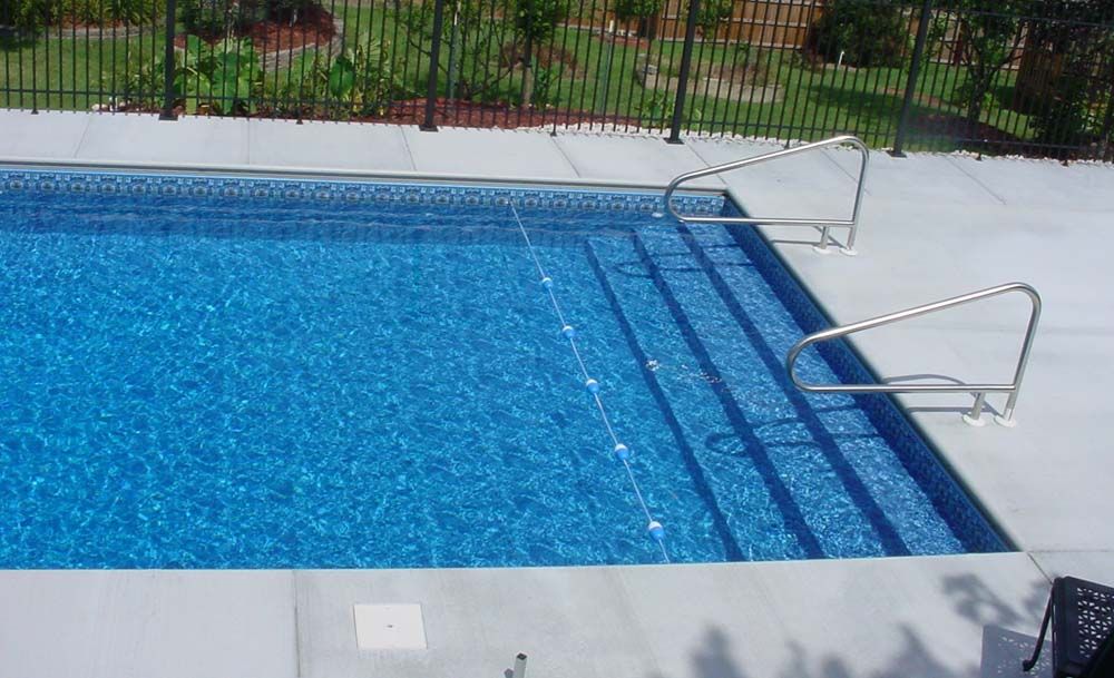 A swimming pool with stairs and a fence in the background