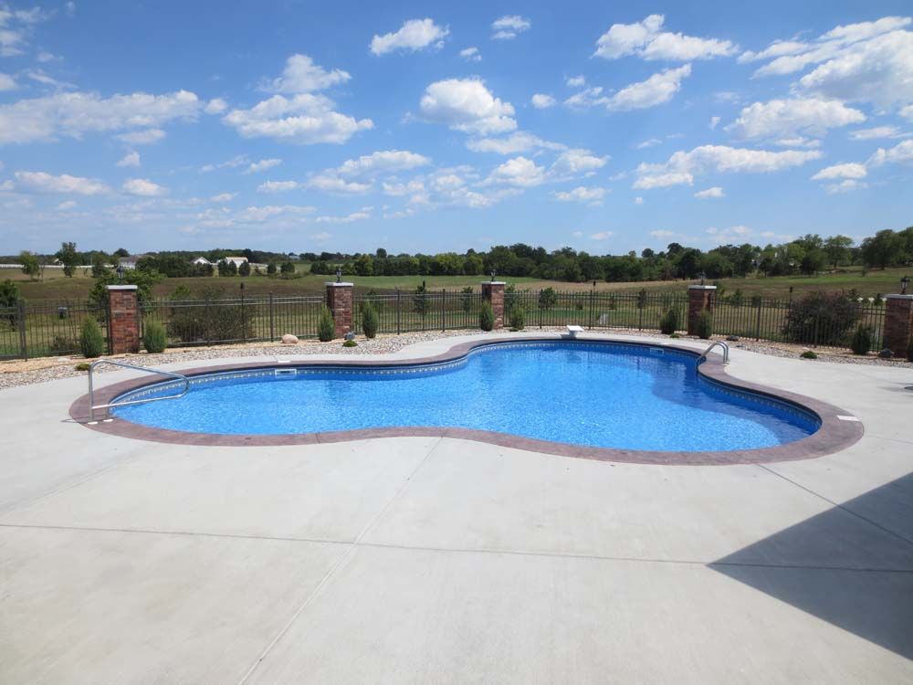 A large swimming pool is surrounded by a concrete patio and a fence.