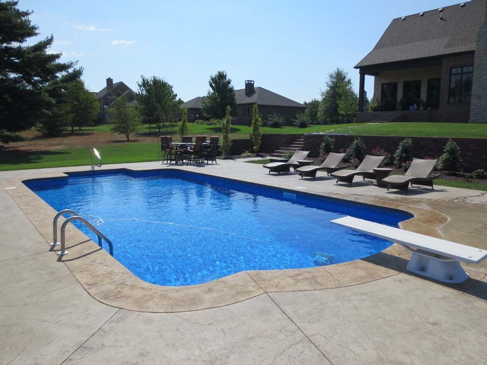 A large swimming pool surrounded by chairs and tables in front of a house