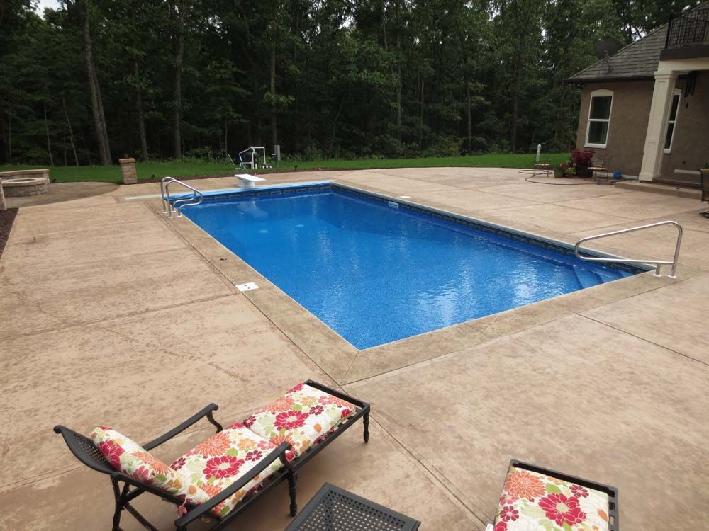 A large swimming pool is surrounded by a concrete patio and chairs.