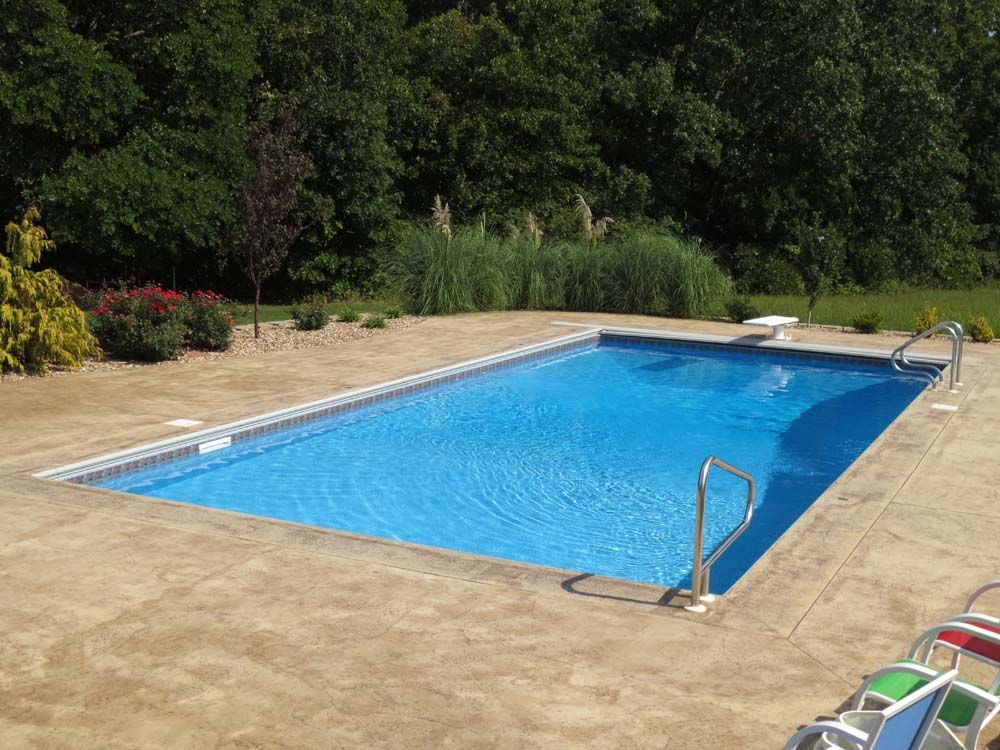 A large blue swimming pool is surrounded by chairs and trees.