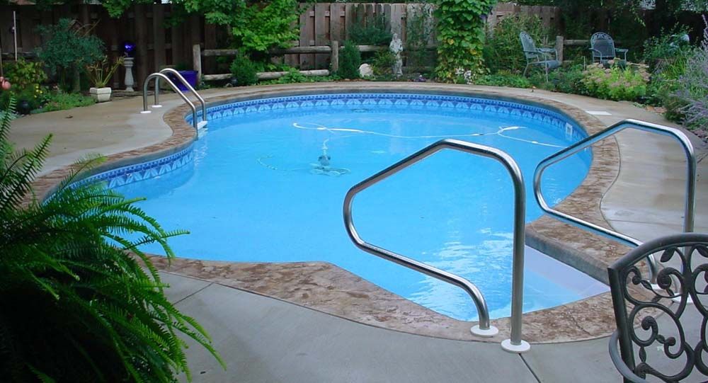 A large swimming pool with stairs leading to it in a backyard.