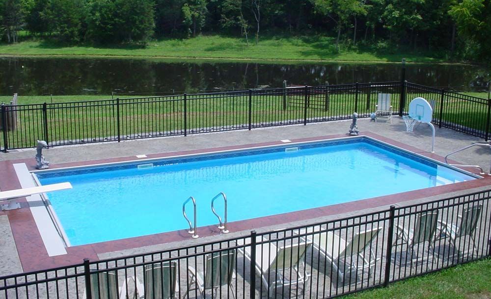 A large swimming pool surrounded by a fence and chairs next to a lake.