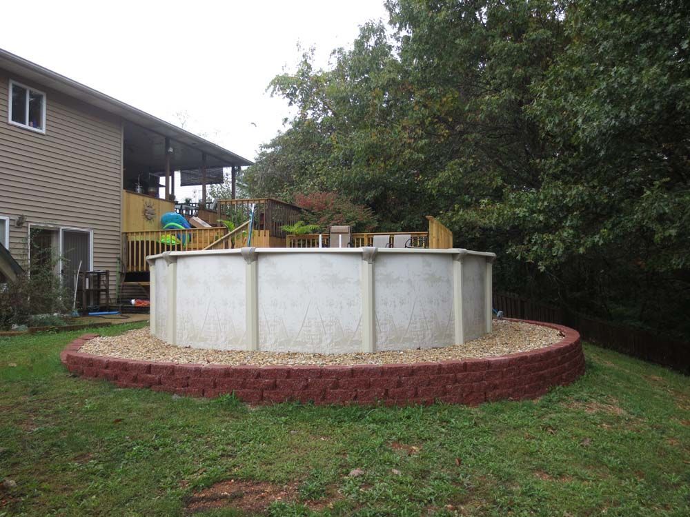 A swimming pool is sitting on top of a brick wall in the backyard of a house.