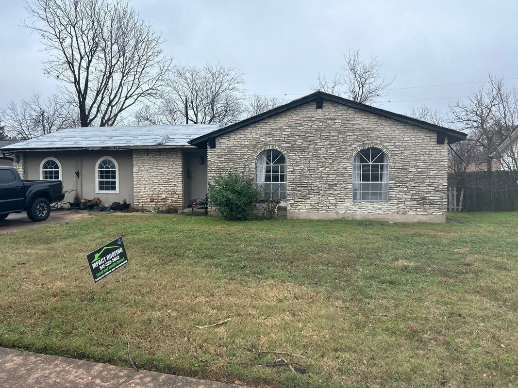 House with stone facade, arched windows, and a green lawn under a cloudy sky.
