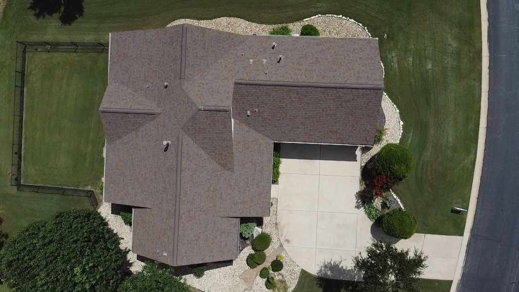 Overhead view of a house with a brown roof, gray driveway, and green lawn.