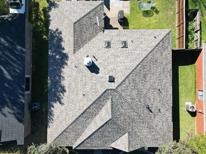 Overhead view of a house with a gray shingle roof, two skylights, a chimney, and satellite dish.