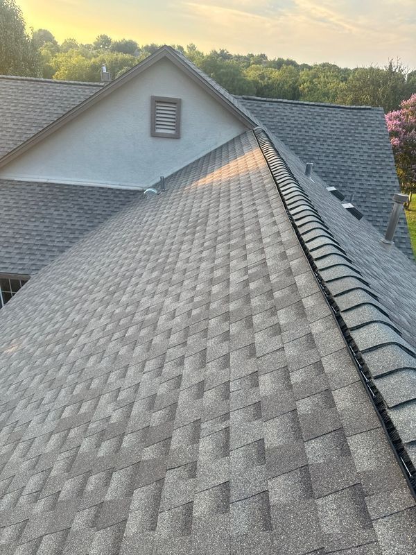 Gray asphalt shingle roof on a house, angled view, overcast sky.