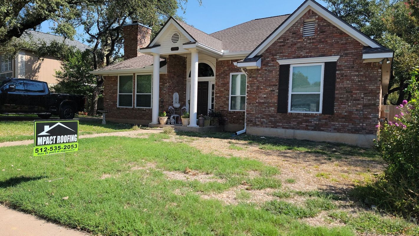 Brick house with a green lawn and a roofing company sign.