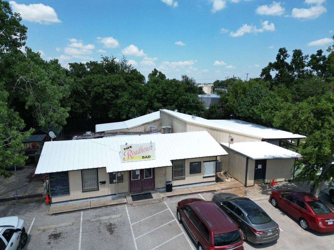 Exterior of a building with a white metal roof, surrounded by trees and parked cars.