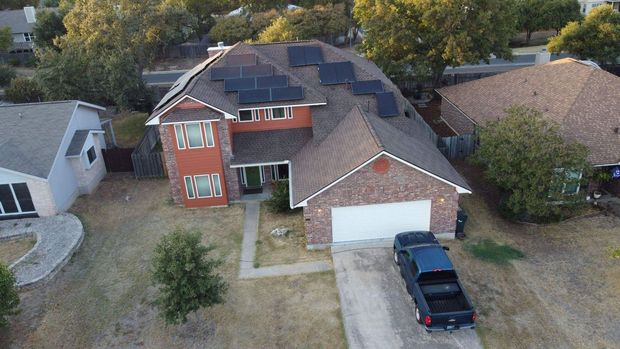 Two-story house with solar panels on roof, red brick facade, and a black truck in the driveway.