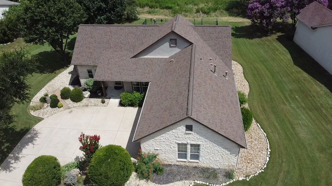 A house with a brown roof and stone facade, surrounded by a lawn and landscaping.