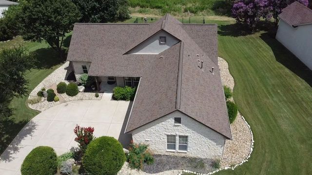 Aerial view of a house with stone siding and brown roof, situated on a green lawn with a driveway.