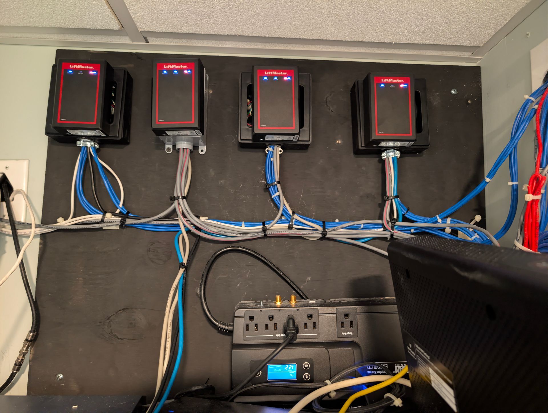 Wall-mounted network equipment with four red-lit devices and cables above a power unit in a utility room