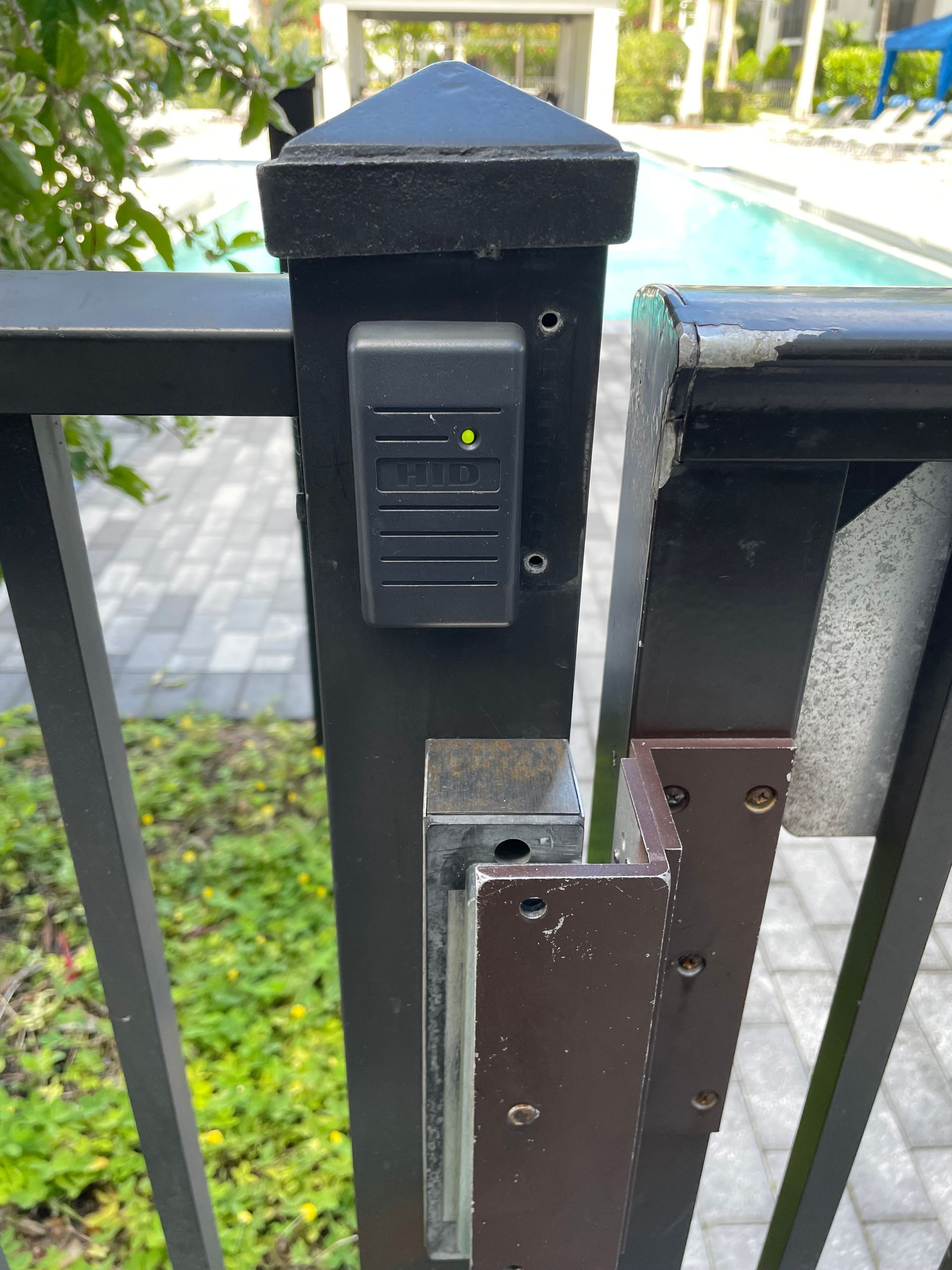 Black metal gate post with a keypad lock beside a pool and patio.