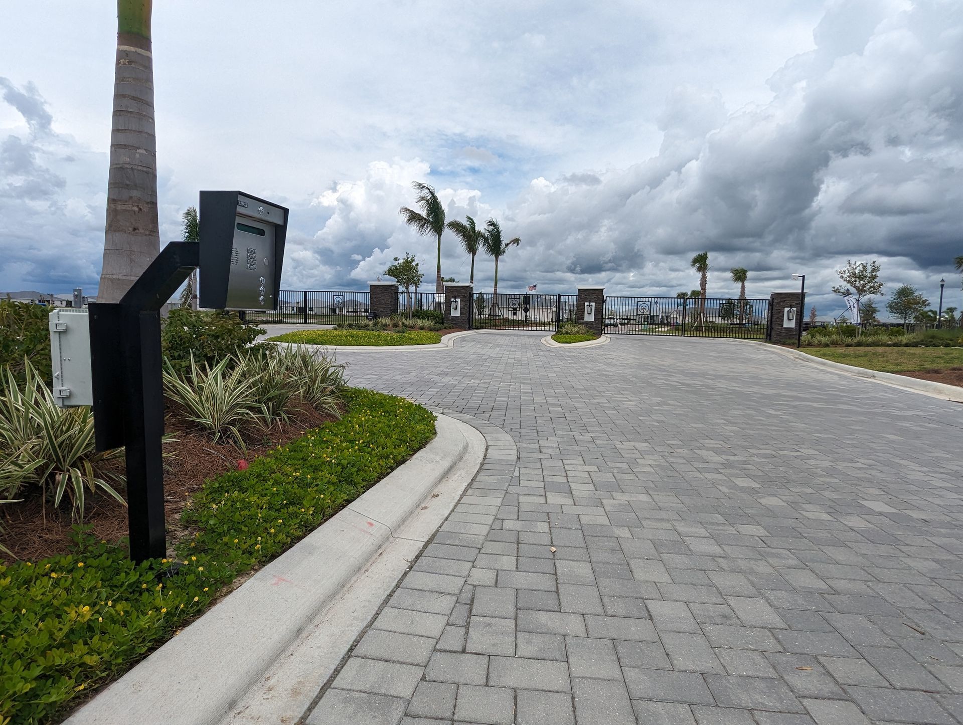 Paved resort entrance with palm trees, landscaped greenery, and cloudy sky