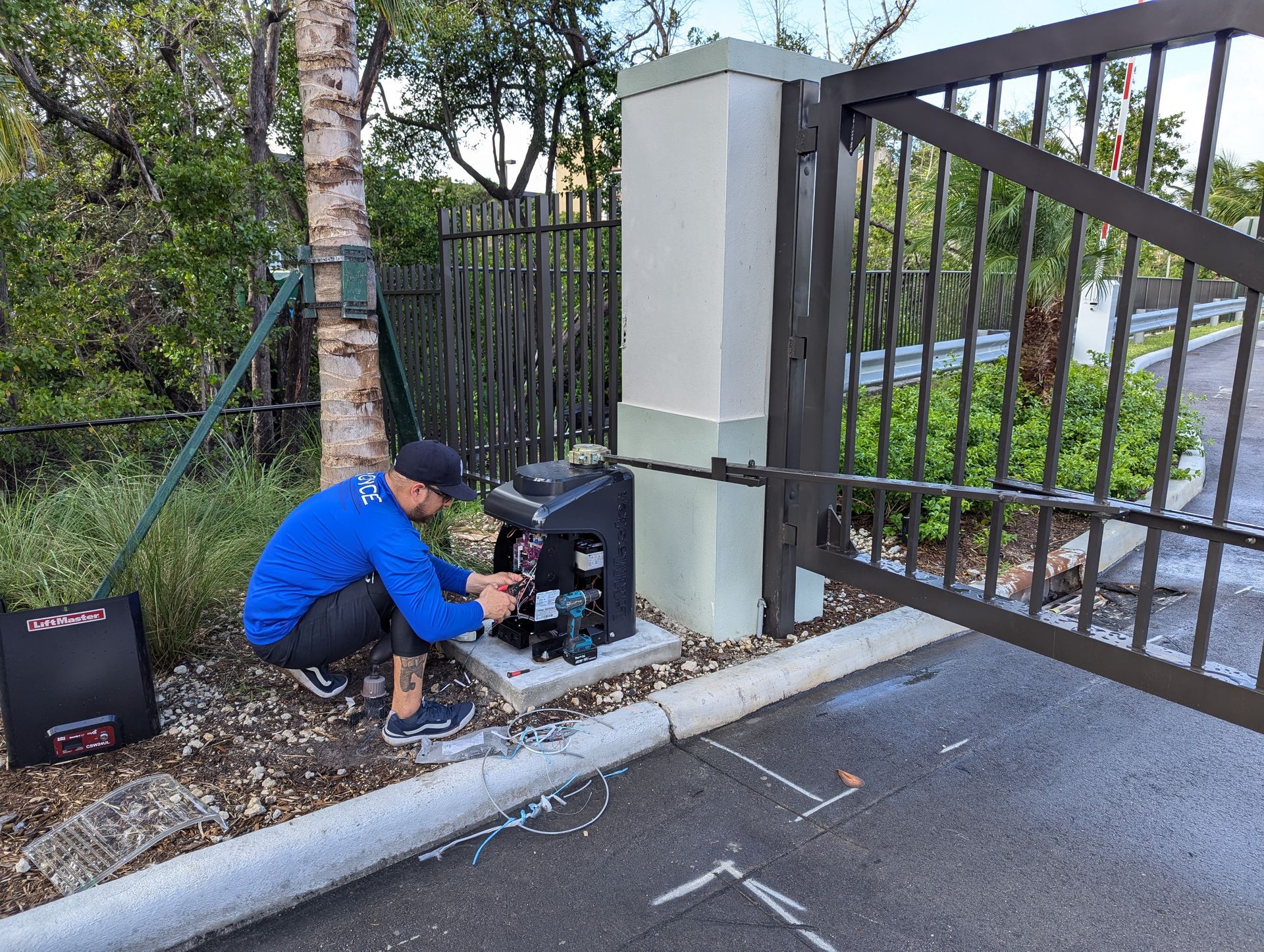 Technician repairing a gate motor beside a driveway entrance.
